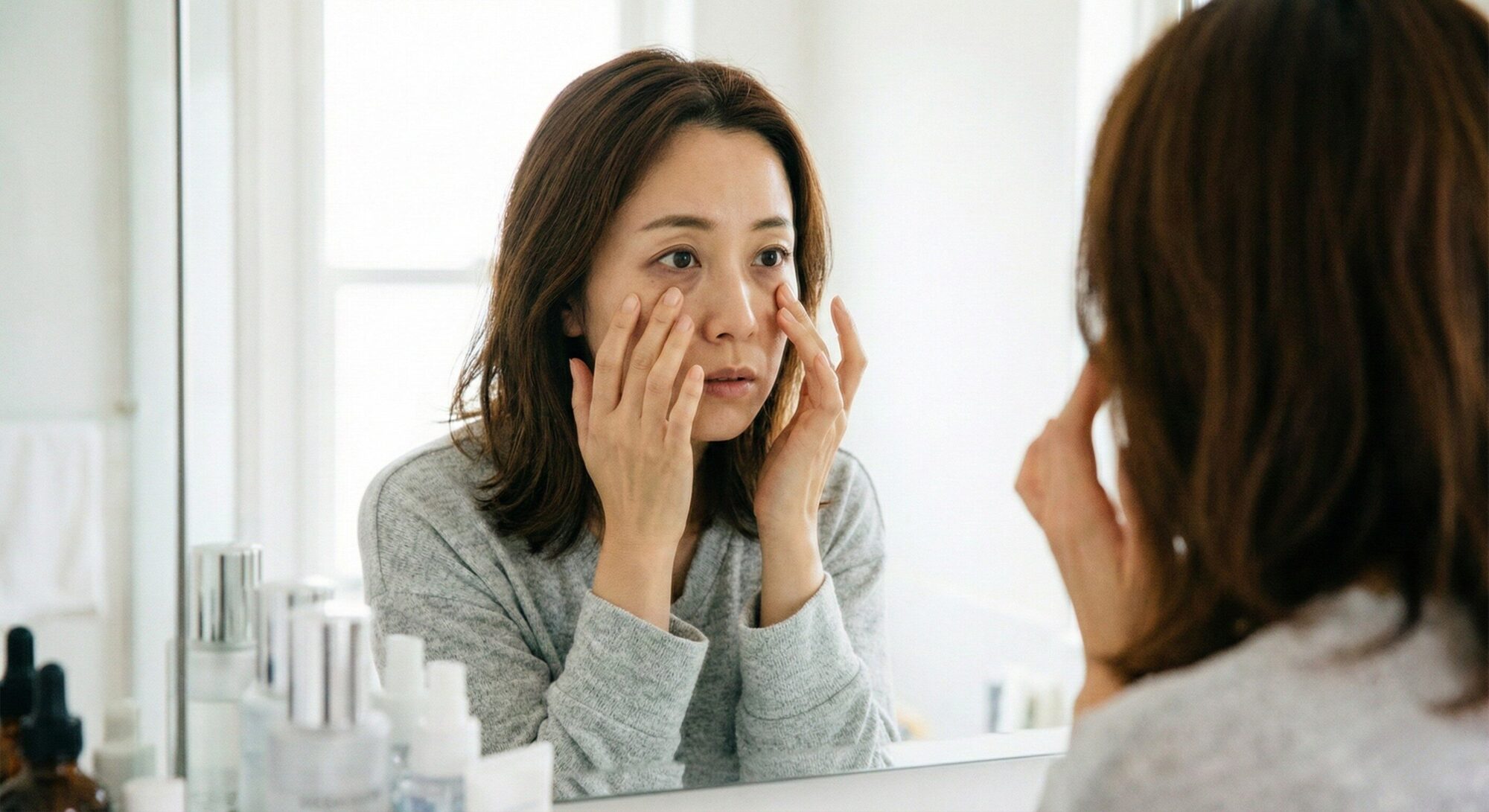 目の下のクマに悩む30代女性が鏡を見ながら気にしている様子、青クマ・茶クマ・黒クマの悩みをイメージ